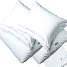 A clean studio shot of a white jersey bedding set, including four fluffy pillows and two folded duvets arranged diagonally against a solid white background.