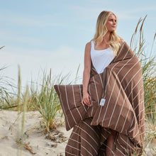 Woman on a beach wrapped in brown jersey bedding with stripes.
