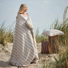 A woman standing on the beach wrapped in beige striped jersey bedding