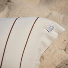Pillow with beige striped jersey pillowcase on a sandy beach.